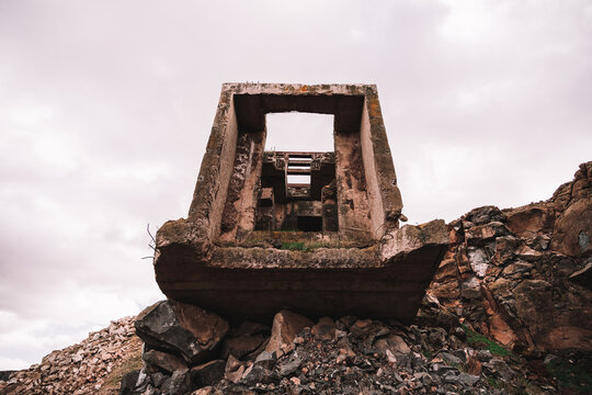 Piece of destroyed cement building on open pit with rough stones under cloudy sky in daylight
