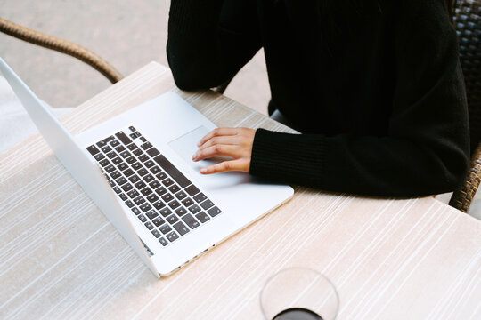 Ethnic woman in black sweater working on netbook at table of sidewalk cafe and typing