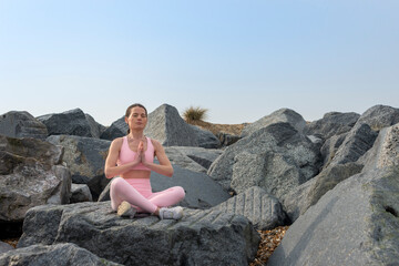 Naklejka na ściany i meble Woman sitting on rocks wearing pink sportswear practicing yoga and meditating.