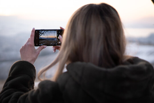 Woman taking photos on her smartphone of a sunset in nature.