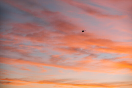 Remote view of helicopter silhouette on background of vivid sundown sky over city in evening