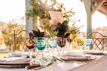 Close-up of served festive table with crystal glasses cutlery napkin on plate near bunch of fresh flowers for wedding and menu card