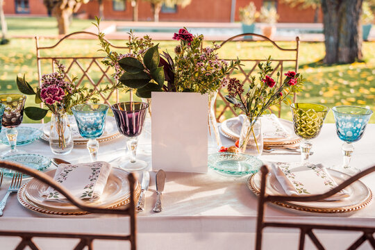 High angle of served festive table with crystal glasses cutlery napkin on plate near bunch of fresh flowers for wedding and menu card