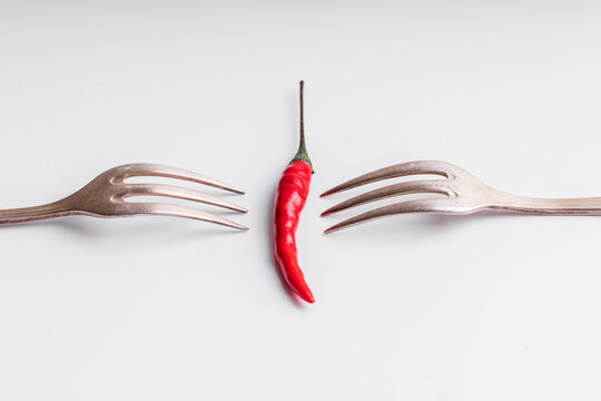 From above of arranged red hot chili peppers with forks on white background