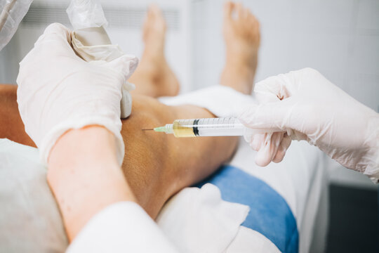 A doctor's hands pricking the knee with a needle while doing an ultrasound test on a patient stretched out on a hospital