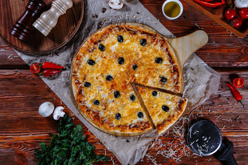 The pizza is on the kitchen table, and the ingredients are scattered around. Cheese pizza with olives
