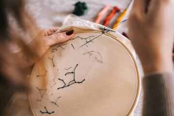 Side view of crop female with hoop and threads embroidering star constellations while sitting at table in light workshop