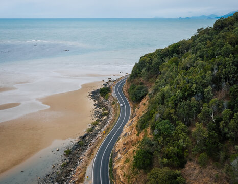 Picturesque drone view car driving along curvy asphalt Great Ocean Road going between hill with lush green trees and ocean sandy beach in Australia