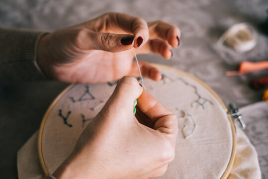 From above crop female with hoop and threads embroidering star constellations while sitting at table in light workshop
