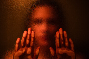 Anonymous blurred female touching glass while standing in dark room with orange illumination