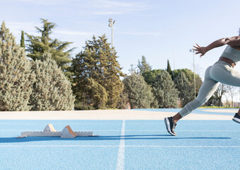 Side view of energetic African American female athlete running out of starting blocks during workout at stadium