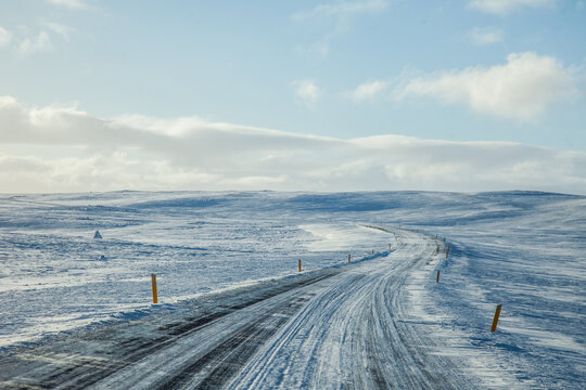Empty roadway running through snowy terrain under blue cloudy sky in winter in Iceland