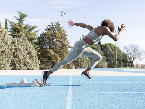 Side view of energetic African American female athlete running out of starting blocks during workout at stadium