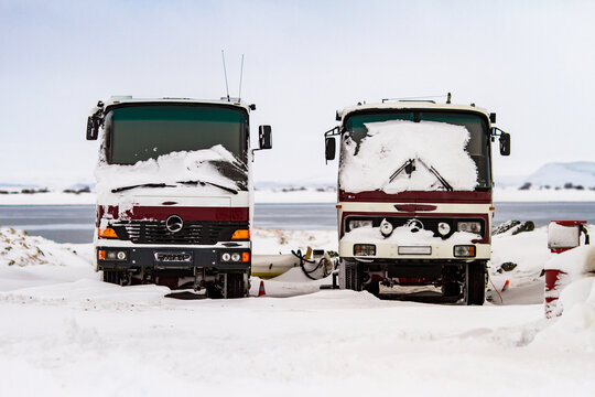 Red trucks covered with snow parked on background of sea in winter in Iceland