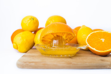 on a wooden board he squeezes fresh oranges with a juicer. Orange juice in a glass close to half of sliced ​​oranges on a white background.