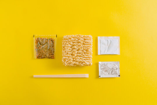Top view layout of uncooked noodles with spices ingredients and sticks in plastic packages on yellow background