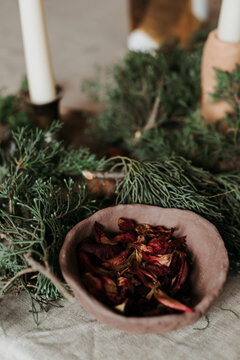 Christmas Composition With Rustic Wooden Bowl Filled With Dried Red Flower Petals Arranged Near Green Fir Branches And Candles On Table