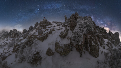 Traveler standing on cliff of snowy mountain range in Picos de Europa National Park under dark starry night sky during winter