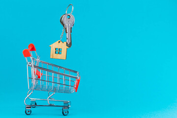 Buying a house or mortgage concept. Model toy house flying with shopping cart on blue background....