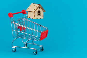 Buying a house or mortgage concept. Model toy house flying with shopping cart on blue background. Housing and Real Estate concept.