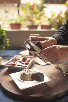 Crop unrecognizable chef sprinkling soft cheese with truffle using grater while cooking at table in house