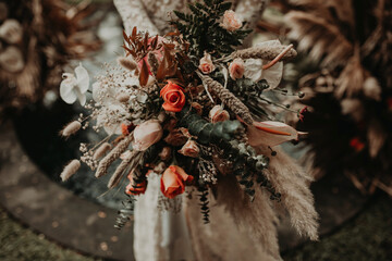 From above of crop unrecognizable female in white wedding dress standing with tender bridal bouquet of various flowers in garden