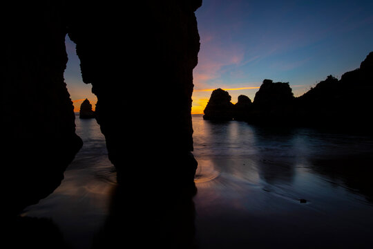 Picturesque view of rocky formations in ocean under cloudy sky at night at Praia do Camilo in Algarve, Portugal