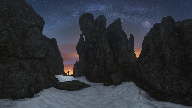 Silhouette of anonymous explorer with flashlight standing between rocky cliffs and admiring dark starry sky in Picos de Europa National Park