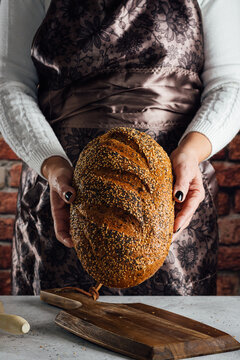 Crop anonymous female baker holding bread with sunflower seeds on table in bakehouse