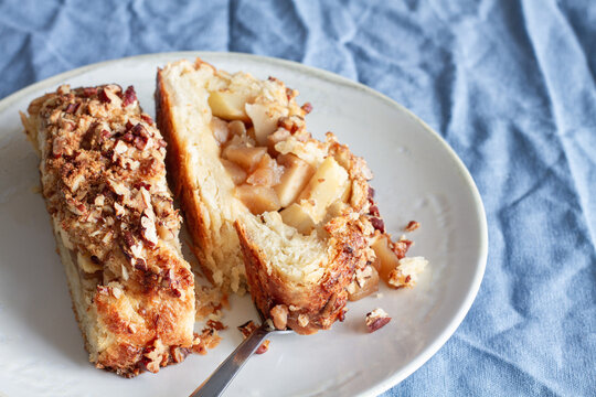 Overhead view of yummy apple pastry on ceramic saucers near fresh fruit and crunchy pecan nuts with flower on creased textile