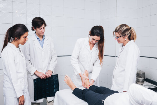 A group of doctors are examining the leg of a patient that is lying on a stretcher on an hospital room while one is holding an x-ray