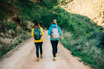 Female hikers in warm clothes walking along sandy road in highlands while enjoying nature and checking time during trekking