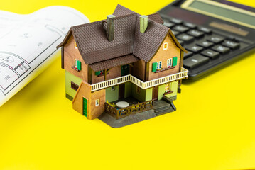 Buying a house or mortgage concept. Model toy house with calculator and plan on yellow background. Housing and Real Estate concept.