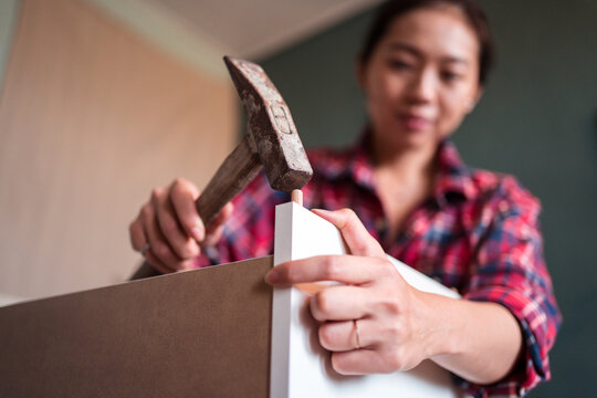 Focused ethnic female using hammer for nailing wooden dowels while assembling new furniture in apartment
