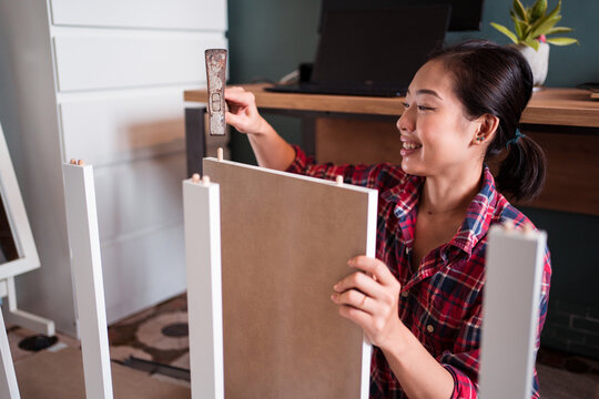 Focused ethnic female using hammer for nailing wooden dowels while assembling new furniture in apartment
