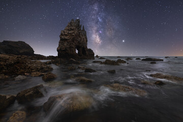 Amazing scenery of sea coast with calm water and rocky cliffs with caves under dark sky with Milky Way