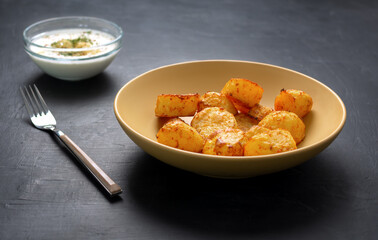 Baked potatoes on a yellow plate, fork and white sauce with garlic on a dark background