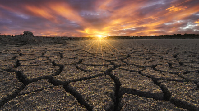 From above of drought cracked lifeless ground under colorful cloudy sky at sunset time