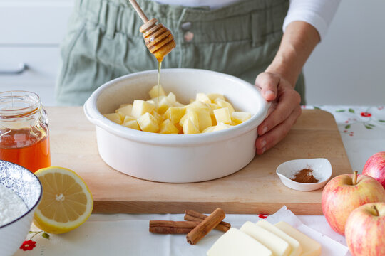 Unrecognizable person adding fresh honey to cut apples in baking pan near flour with lemon and butter with cinnamon during crumble preparation at home