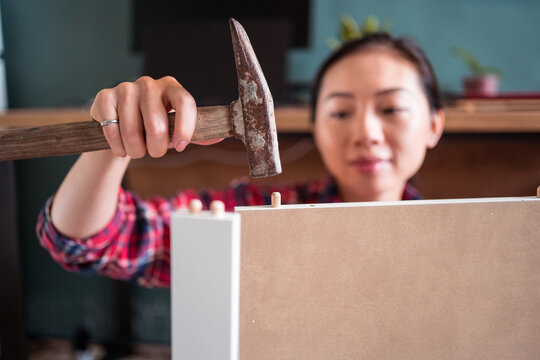 Focused ethnic female using hammer for nailing wooden dowels while assembling new furniture in apartment