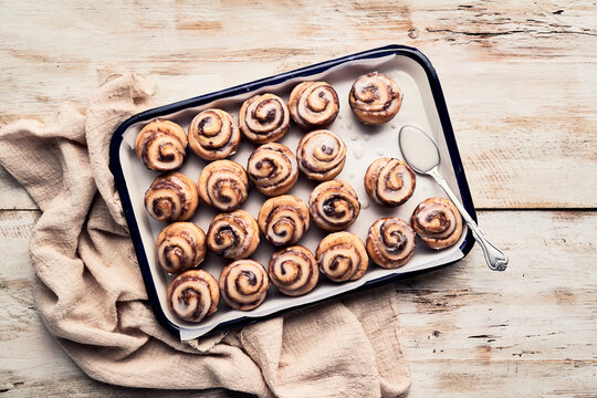 Top view of many glazed cinnamon rolls placed in rows on baking tray on wooden table