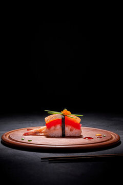Appetizing sushi Nigiri with salmon and prawn served on round wooden board on table with chopsticks on black background