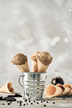 Scoops of chocolate ice cream in waffle cones in metal bucket placed on table