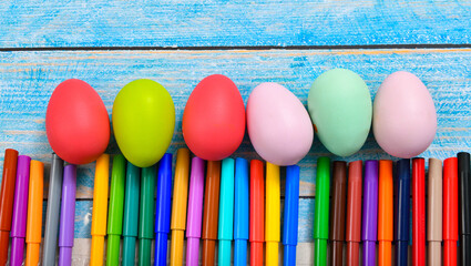 Painted Easter eggs and colored markers lie on a blue wooden table.