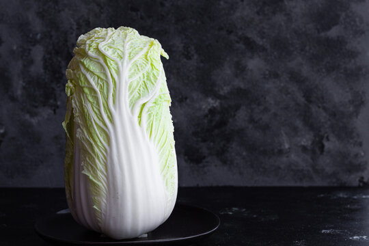 Ripe green Chinese cabbage served on plate on table on black background in studio