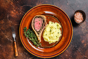 Beef Wellington pastry with mushed potato on a rustic plate. Dark background. Top view