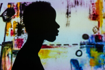 Silhouette of unrecognizable ethnic person standing against wall with projection of abstract painting