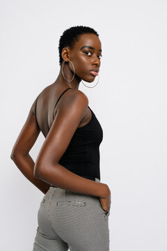 Side view of slim African American female with hands in pockets looking at camera over shoulder against gray background
