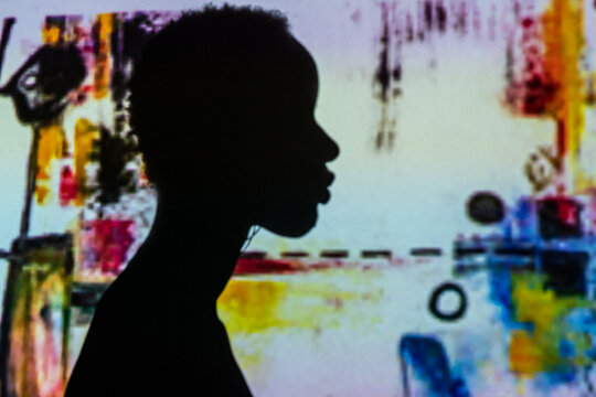 Silhouette of unrecognizable ethnic person standing against wall with projection of abstract painting