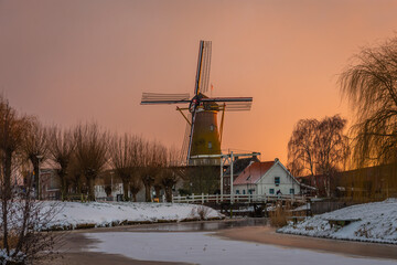 Winter dutch scenery with a traditional windmill along the frozen canal during colorful sunset in Etten-Leur, North Brabant